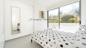 Un dormitorio con una cama, un ventanal grande, un espejo y un cuadro en la pared.