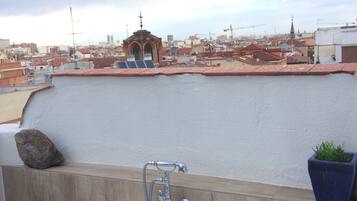 Una terraza en la azotea con una bañera, una planta en maceta y vistas a un paisaje urbano.