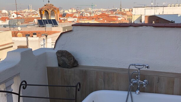 A rooftop terrace with a bathtub, a stone wall, and a view of the cityscape. - Penthouse with terraces in Gran Via (Madrid)