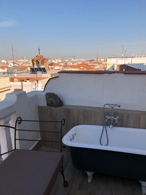 A rooftop terrace with a bathtub, a stone wall, and a view of the cityscape. - Penthouse with terraces in Gran Via (Madrid)