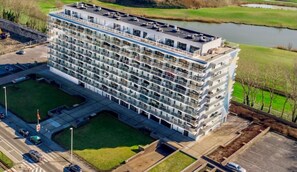 Un hôtel à plusieurs étages au design moderne, doté de balcons à chaque niveau et d’un espace de stationnement à l’avant.