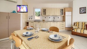 A modern kitchen with wooden cabinets, a dining table set for two, and a sofa in the living area. - Front Beach Posto Vecchio 2 by LoveSud (Pescoluse)