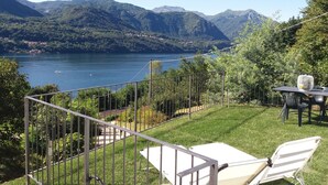 Una terraza con vistas a un lago y montañas, una silla blanca y una mesa con un ventilador.