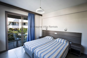 A modern bedroom with a large bed, a nightstand, a ceiling light, and a sliding glass door leading to a balcony.