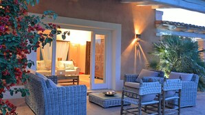 An outdoor seating area with wicker furniture, a laptop on a table, and a door leading to an interior space.