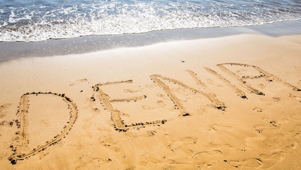 Une plage de sable sur laquelle on a écrit le mot « DENIA » dans le sable.
