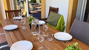 Une table de salle à manger en bois, mise avec des assiettes, des verres et des couverts, entourée de chaises et agrémentée d’une plante en pot.
