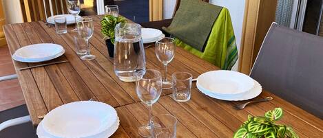 A wooden dining table set with plates, glasses, and cutlery, surrounded by chairs and a potted plant.