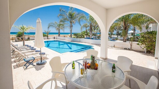 A poolside area with a glass table, chairs, and a view of the sea. - Ayia Napa Holiday Villa SV11 - Stunning 3BDR Seafront Ayia Napa Villa with Pool (Unknown)