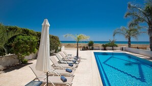 A poolside area with lounge chairs and an umbrella, overlooking a beach and the ocean. - Ayia Napa Holiday Villa SV11 - Stunning 3BDR Seafront Ayia Napa Villa with Pool (Unknown)