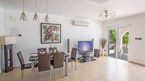 A modern dining area with a table set for four, a television, and a large abstract painting on the wall. - Ayia Napa Holiday Villa SV11 - Stunning 3BDR Seafront Ayia Napa Villa with Pool (Unknown)