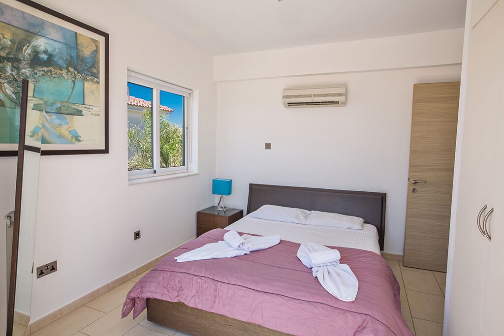 A bedroom with a bed, a window, an air conditioner, a nightstand, and a painting.