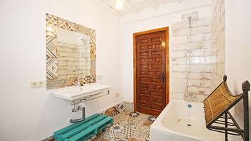 Ein Badezimmer mit einem weißen Waschbecken, einer Holztür und einer Badewanne.
