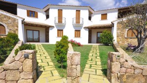 A white building with stone walls, wooden shutters, and a paved pathway leading to the entrance.