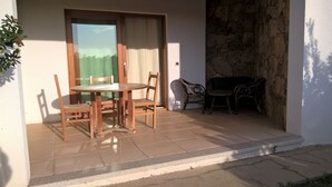 A patio with a wooden table and chairs, a wicker sofa, and a stone wall.