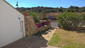 A stone wall with potted plants, a concrete pathway, and a view of a hillside with trees.