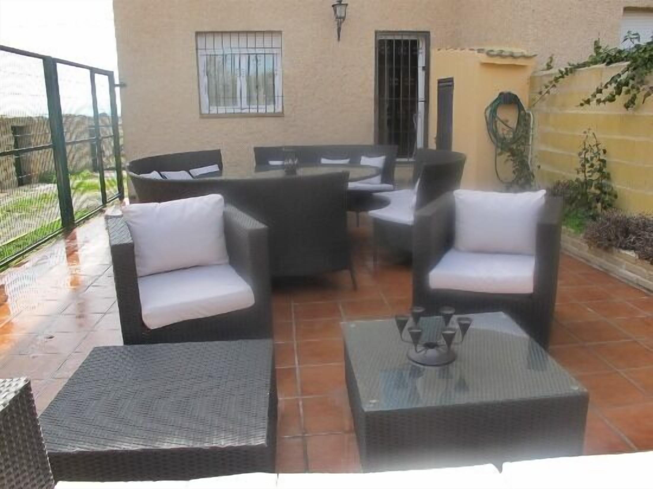 Une terrasse extérieure aménagée avec des meubles en osier, notamment deux fauteuils et une petite table, ainsi qu’une table ronde avec des chaises.