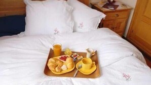 A neatly made bed with white linens, a wooden headboard, and a bedside table with a lamp and a book.