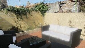 An outdoor patio with wicker furniture, including a sofa and chairs, and a glass-top table.