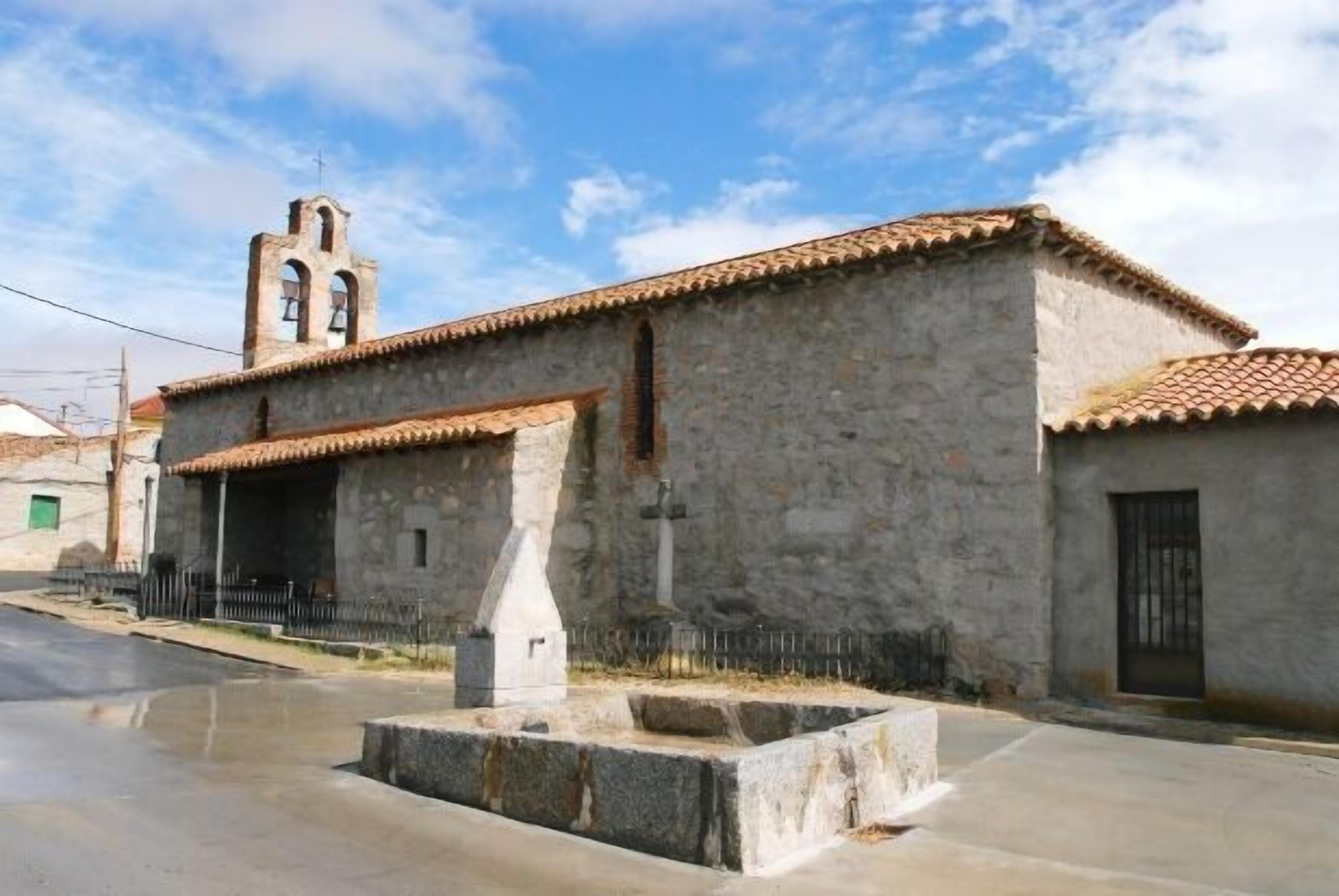 A stone building with a bell tower, a small courtyard, and a paved street.