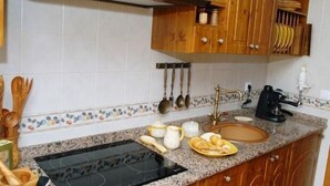 A kitchen with a granite countertop, a stove, wooden cabinets, and various kitchen utensils.