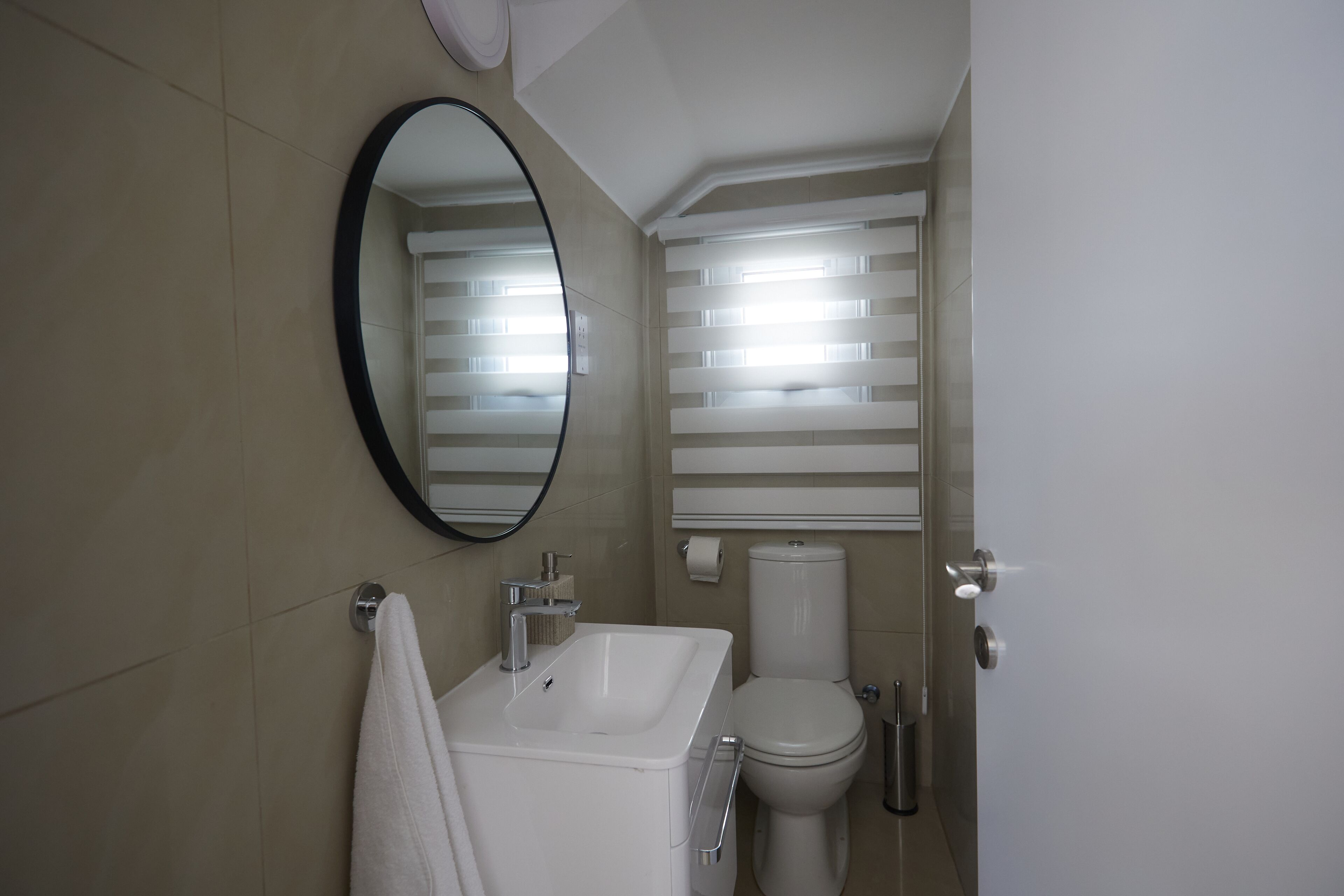 Ein Badezimmer mit einem weißen Waschbecken, einem Spiegel, einer Toilette und einem an der Wand hängenden Handtuch.