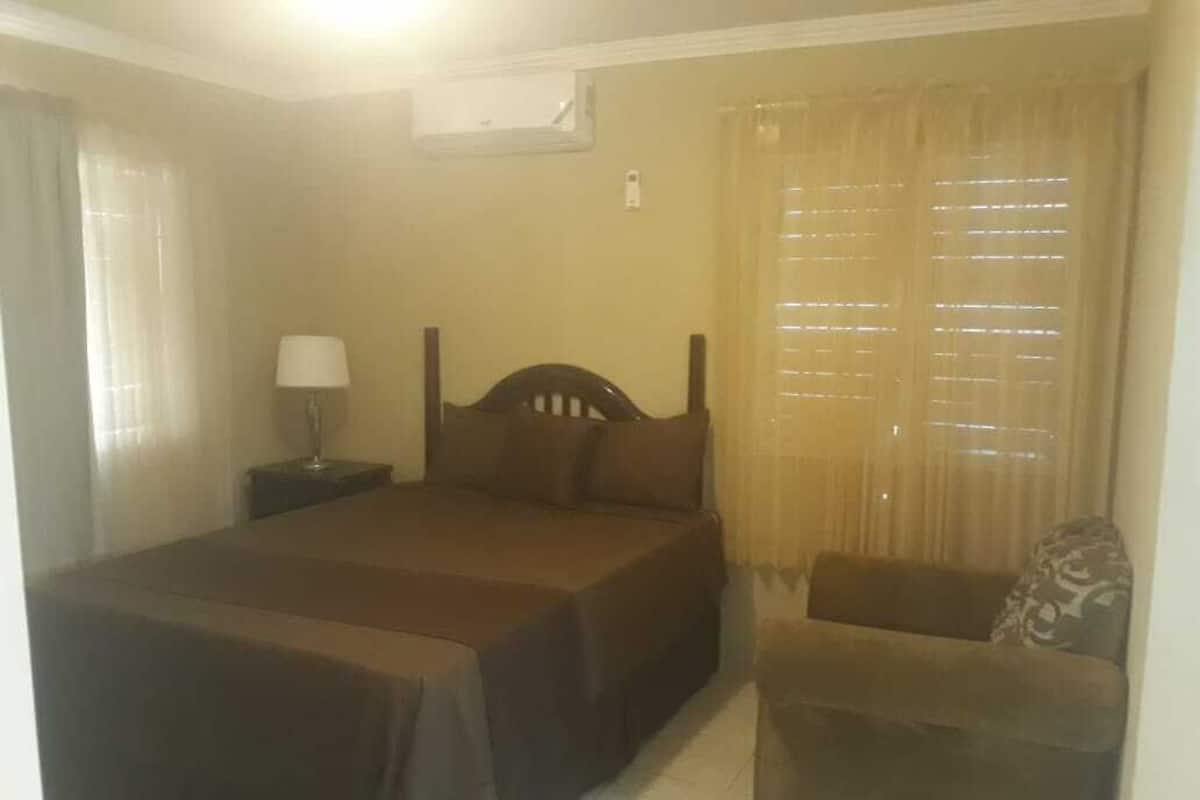 A bedroom with a bed, a nightstand, a chair, and a window with curtains.