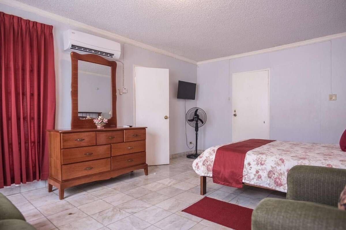 A bedroom with a bed, dresser, mirror, TV, and fan.