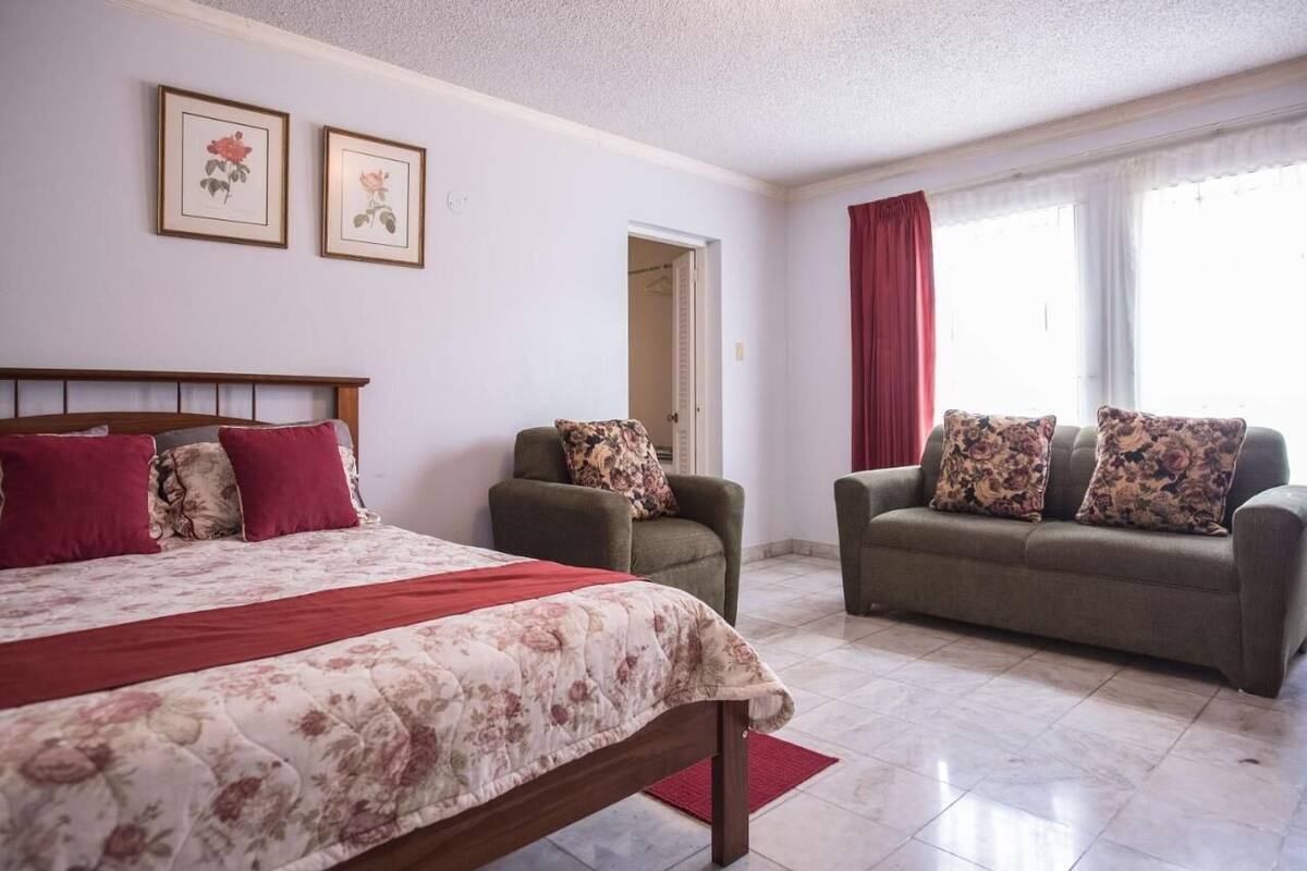 A bedroom with a bed, two chairs, a sofa, and a window with curtains.
