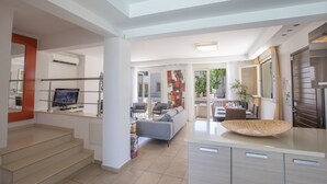 Et moderne opholdsområde med trappe, sofa, spisebord og køkkenø.