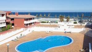 Una piscina con borde curvo, rodeada por una cerca blanca y algunas sillas de descanso.