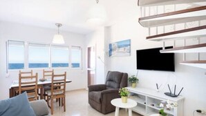 Una sala de estar moderna con un sofá, una mesa de comedor con sillas, un televisor montado en la pared y una escalera.