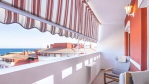 Un balcón con toldo a rayas, vista al mar y una silla con cojín.