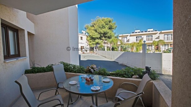 Ein Balkon mit rundem Tisch und Stühlen, Blick auf angrenzende Gebäude und einen Baum.