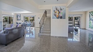 A spacious living area with a modern design, featuring a staircase, a large painting, and a seating area with a sofa and chairs.