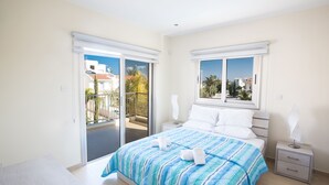 A bedroom with a bed, a nightstand, a bedside lamp, and a view of the outside.