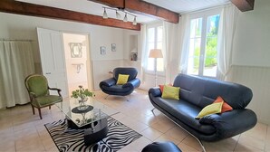 Un salon avec une table basse en verre, un canapé noir orné de coussins jaunes, un fauteuil vert et un tapis à motifs zébrés.