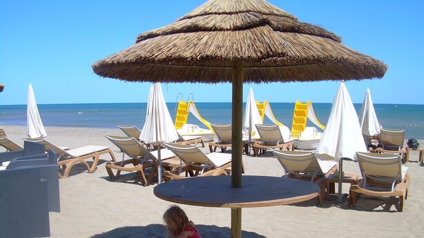 Une plage avec des chaises longues, des parasols et une structure en forme de parasol recouverte de chaume.