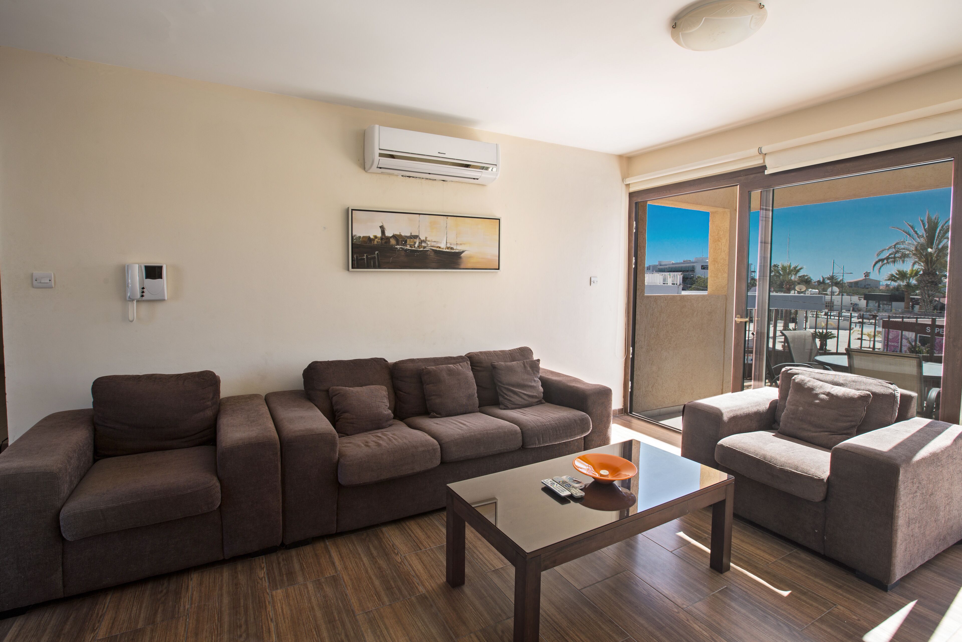 A modern living room with a brown sofa, a small table, and a view of the city through large windows.