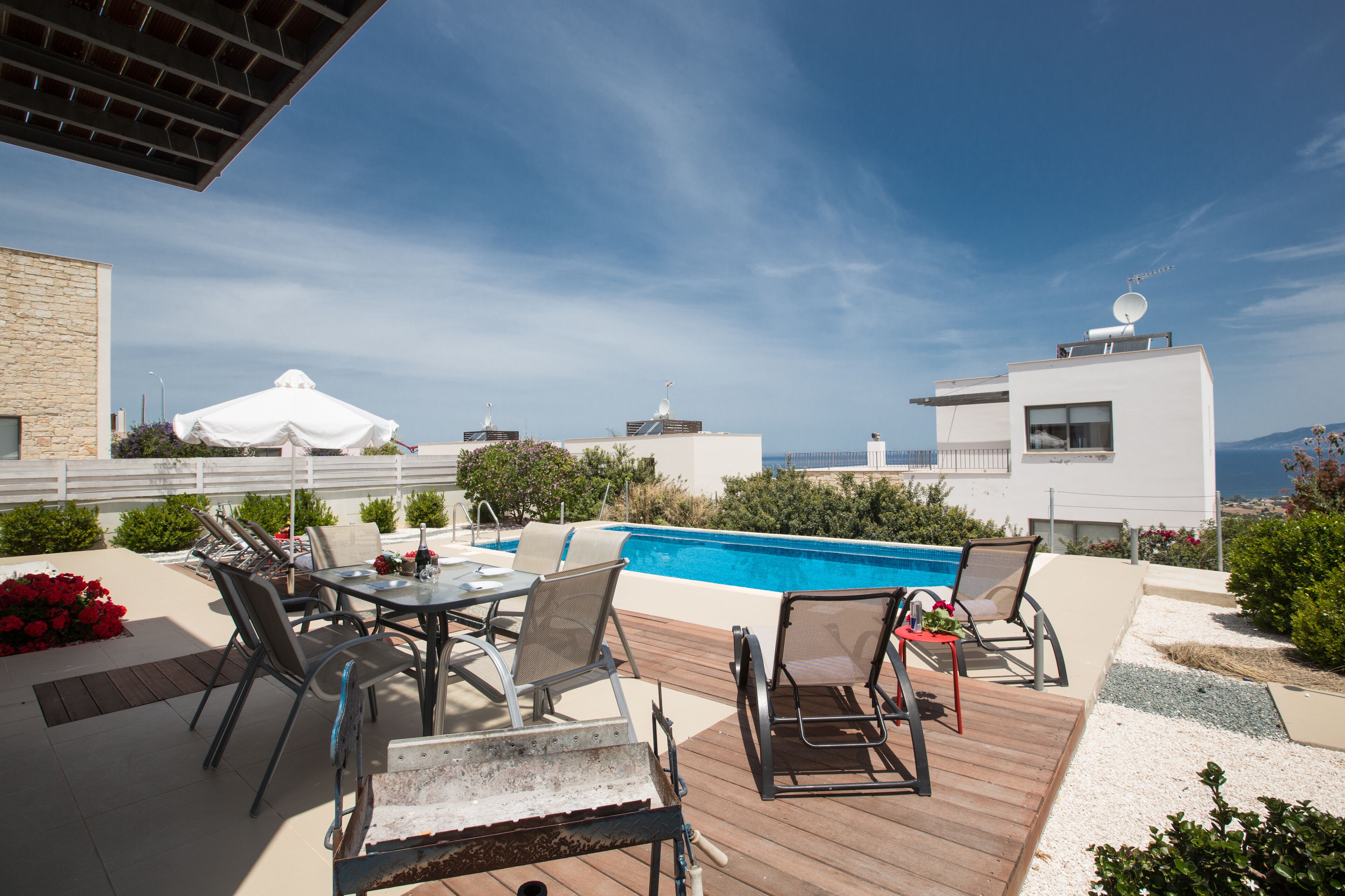 A rooftop pool area with a view of the sea, outdoor seating, and a modern building in the background.