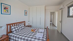 Makuuhuoneessa on ruutukuviollinen päiväpeite, yöpöytä lampun kanssa, kehystetty kuva vihanneksista ja liukuovilla varustettu vaatekaappi.