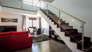 Een moderne woonkamer met een rode bank, een eethoek met een tafel en stoelen, en een trap met glazen balustrades.