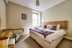 Een slaapkamer met een bed, een bureau, een radiator en een raam.