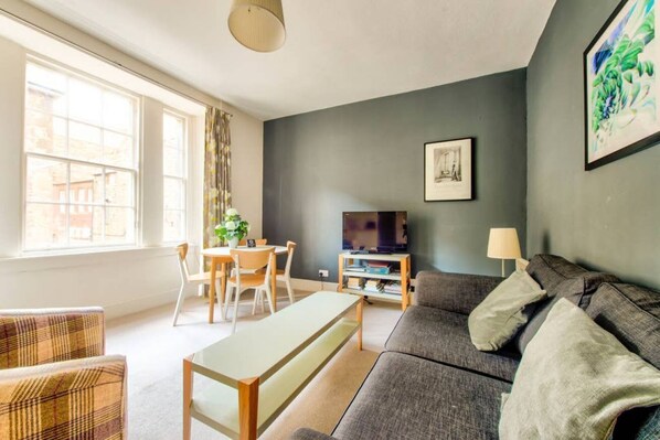 Een woonkamer met een bank, een eettafel met stoelen, een televisie en een lamp.