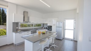 Eine moderne Küche mit weißen Schränken, einer zentralen Kochinsel mit Barhocker, einem eingebauten Backofen und einem Kühlschrank.