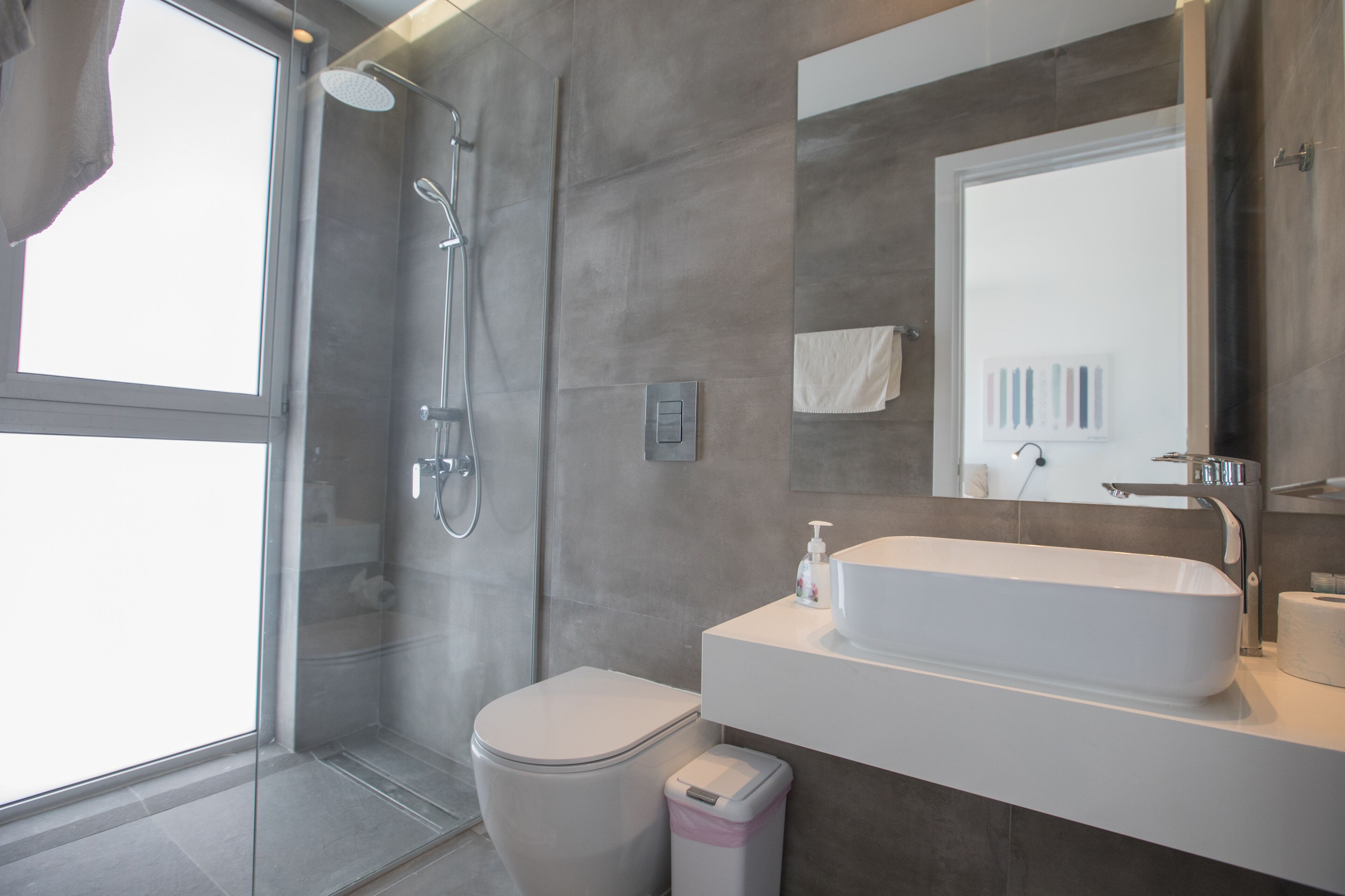 A modern bathroom with a glass-enclosed shower, a white toilet, and a large sink with a mirror above it.