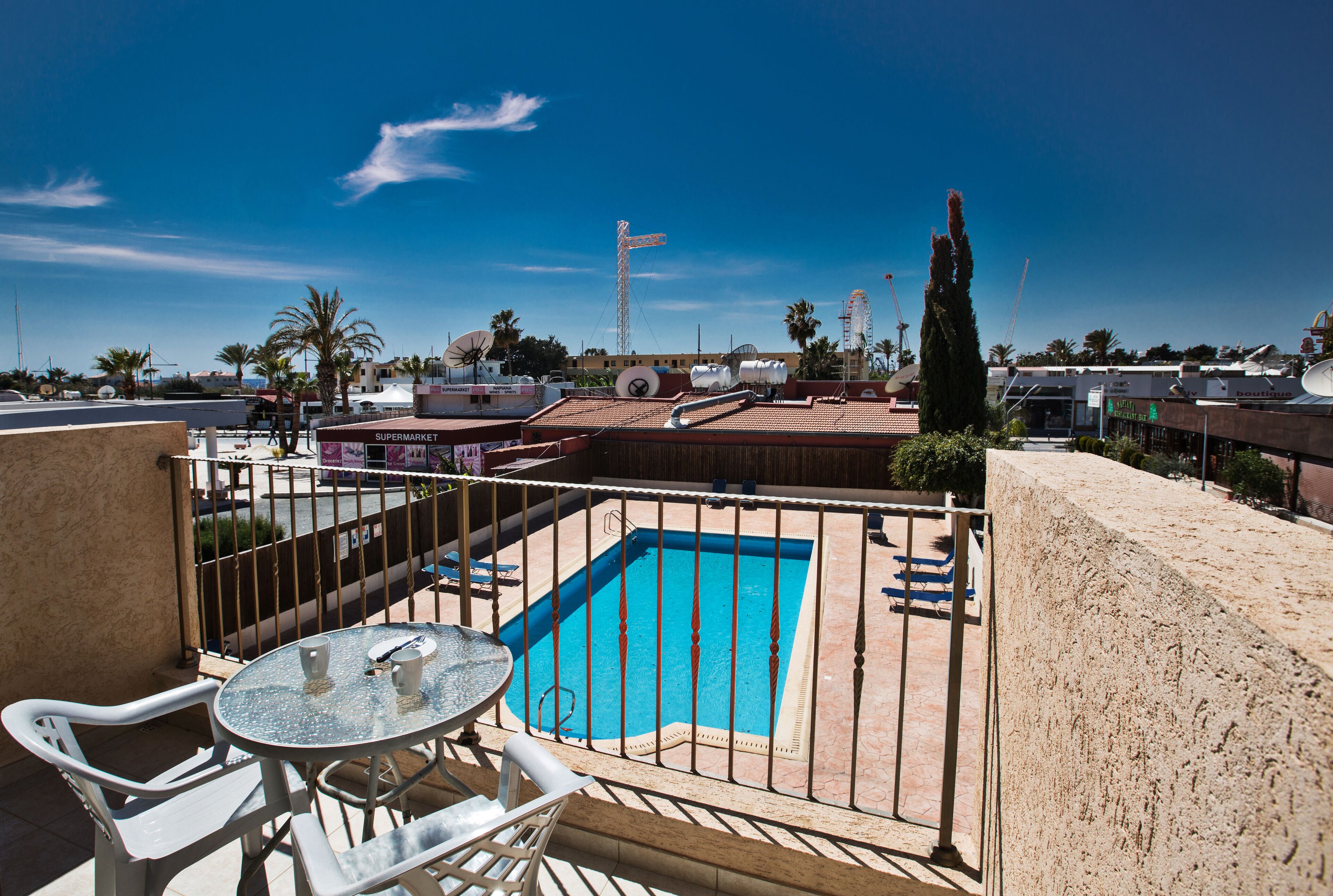 A rooftop pool area with a table and chairs, surrounded by a fence.