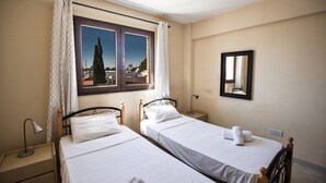 Une chambre d’hôtel avec deux lits simples, une table de chevet avec une lampe, une fenêtre avec des rideaux et un miroir au mur.