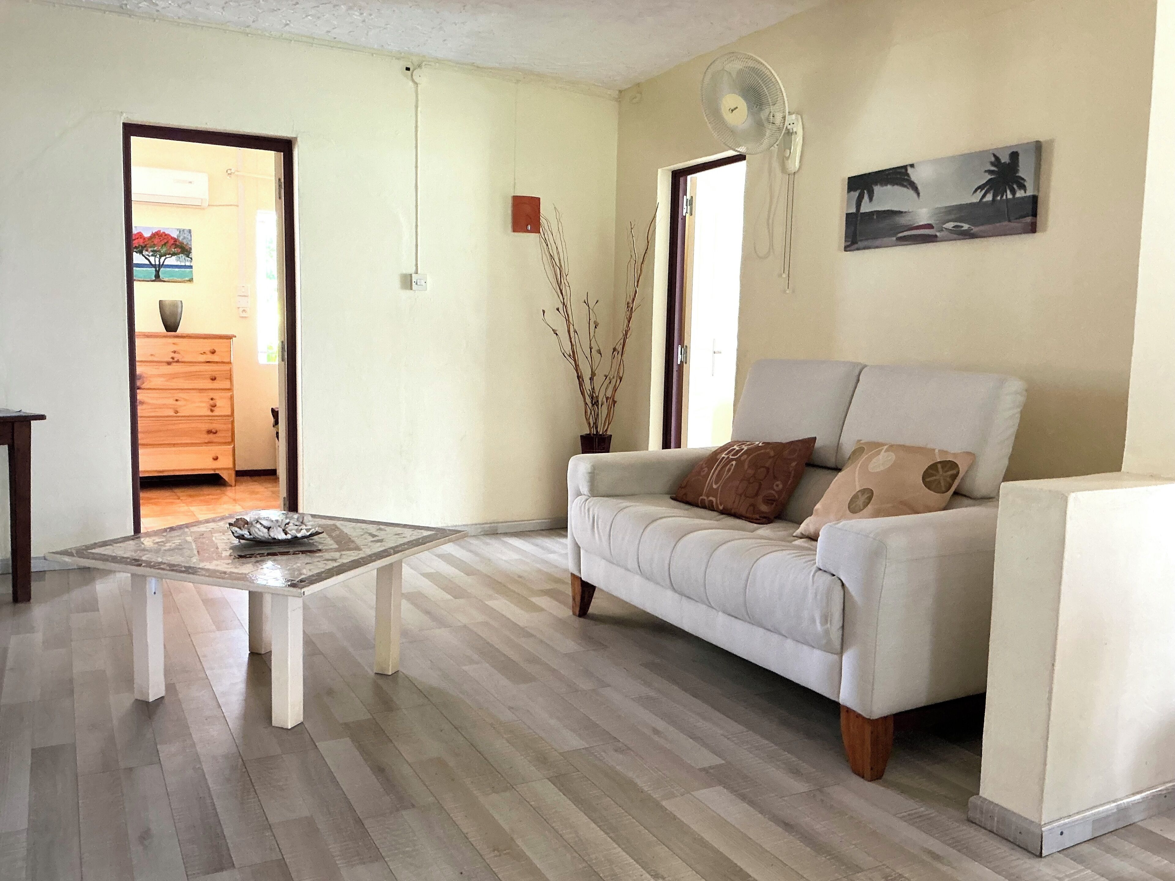 Un salon avec un canapé, une table basse, un ventilateur et un tableau accroché au mur.