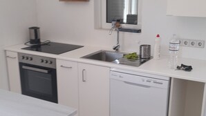 Kompakti keittiö, jossa on valkoiset kaapit, sisäänrakennettu uuni, astianpesukone ja pesuallas.